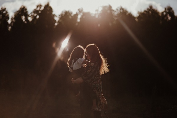 mother holding child with trees in the background and the sun shining on them